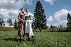 Two stylish women in elegant outfits posing outdoors in a scenic landscape.
