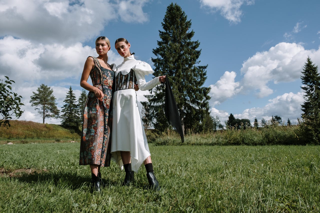 Two stylish women in elegant outfits posing outdoors in a scenic landscape.